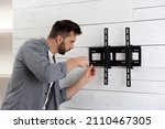 Man with screwdriver installing TV bracket on wall indoors