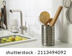 Holder with cooking utensils near sink on kitchen counter