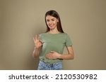 Healthy woman holding hand on belly and showing OK gesture against beige background
