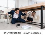 Scared employees hiding under office desk during earthquake