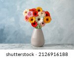 Bouquet of beautiful colorful gerbera flowers in vase on white marble table against light blue background