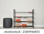Shoe rack with different pairs of rubber slippers near white wall indoors