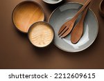 Stylish empty dishware and wooden cutlery on brown background, flat lay