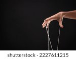 Woman pulling strings of puppet on black background, closeup. Space for text