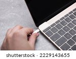 Woman plugging USB cable with type C connector into laptop port at grey table, closeup