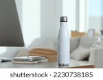 Stylish thermo bottle on wooden table at workplace in office