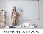 Happy young teacher explaining something at whiteboard in classroom. Space for text
