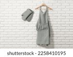 Clean kitchen apron with pattern and oven gloves on white brick wall. Space for text