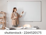 Happy young teacher explaining something at whiteboard in classroom. Space for text