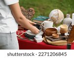Woman holding beautiful bowls near table with different items on garage sale, closeup