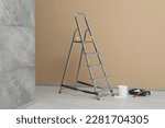 Metallic folding ladder and painting tools near beige wall indoors