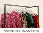 Clothing rack with colorful sequin party dresses on hangers near white wall indoors, closeup