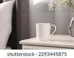 Ceramic mug on white bedside table indoors. Mockup for design