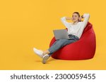 Small photo of Happy woman with laptop sitting on beanbag chair against orange background. Space for text