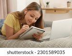Teenage girl writing in notebook on bed at home