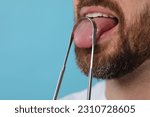 Man brushing his tongue with cleaner on light blue background, closeup. Space for text
