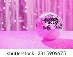 Shiny disco ball on table against blurred background, toned in pink. Space for text