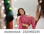 Beautiful young woman with pink sequin dress near mirror in boutique. Choosing party clothes