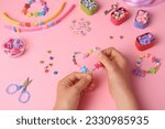 Child making beaded jewelry and different supplies on pink background, above view. Handmade accessories