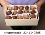 Woman holding box of delicious chocolate candies on dark background, closeup