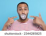 Small photo of Portrait of young man blowing bubble gum on light blue background