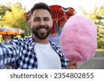 Happy young man with cotton candy taking selfie at funfair