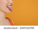 Happy woman showing her tongue on orange background, closeup. Space for text