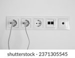 Small photo of Many power sockets with plugs, ethernet and TV coax plates on white wall indoors