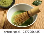 Small photo of Cup of fresh green matcha tea with whisk and spoon on bamboo mat, closeup