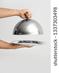Small photo of Hands of waiter with tray and cloche on light background