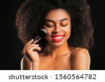 Portrait of beautiful African-American woman with makeup brush on dark background