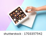 Woman taking chocolate candy from box on color background