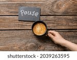 Woman with cup of coffee and word PAUSE on wooden background