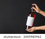 Hands holding bottle of wine with blank label on dark background. Mockup for design