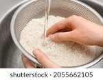 Small photo of Woman rinsing rice in sifter under running water, closeup