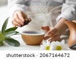 Woman adding essential oil to aroma diffuser on table