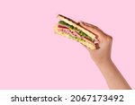 Female hand with tasty sandwich on color background