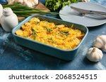Baking dish of tasty potato with cheese and garlic on color background