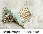 Box with stylish jewelry and bouquet of beautiful flowers on grunge background