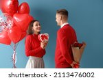 Young man greeting his girlfriend for Valentine's Day on color background