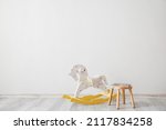 Small photo of Rocking horse and stool with books near light wall