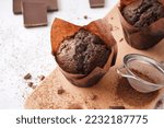 Wooden board with tasty chocolate muffins on light background, closeup