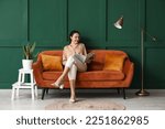 Young woman reading magazine on red sofa near green wall