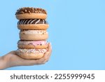 Female hand with stack of tasty donuts on color background, closeup