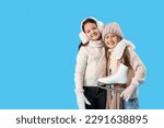 Little girls in winter clothes with ice skates hugging on blue background