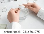 Small photo of Woman cleaning beautiful ring with toothbrush on light background, closeup
