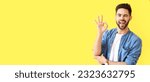 Small photo of Happy young man showing OK on yellow background with space for text