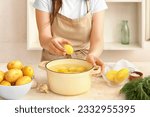 Small photo of Woman putting peeled potato in pot at table in kitchen