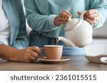 Young woman pouring hot tea for her mother in kitchen, closeup