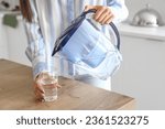 Young woman pouring water from filter jug into glass in kitchen, closeup